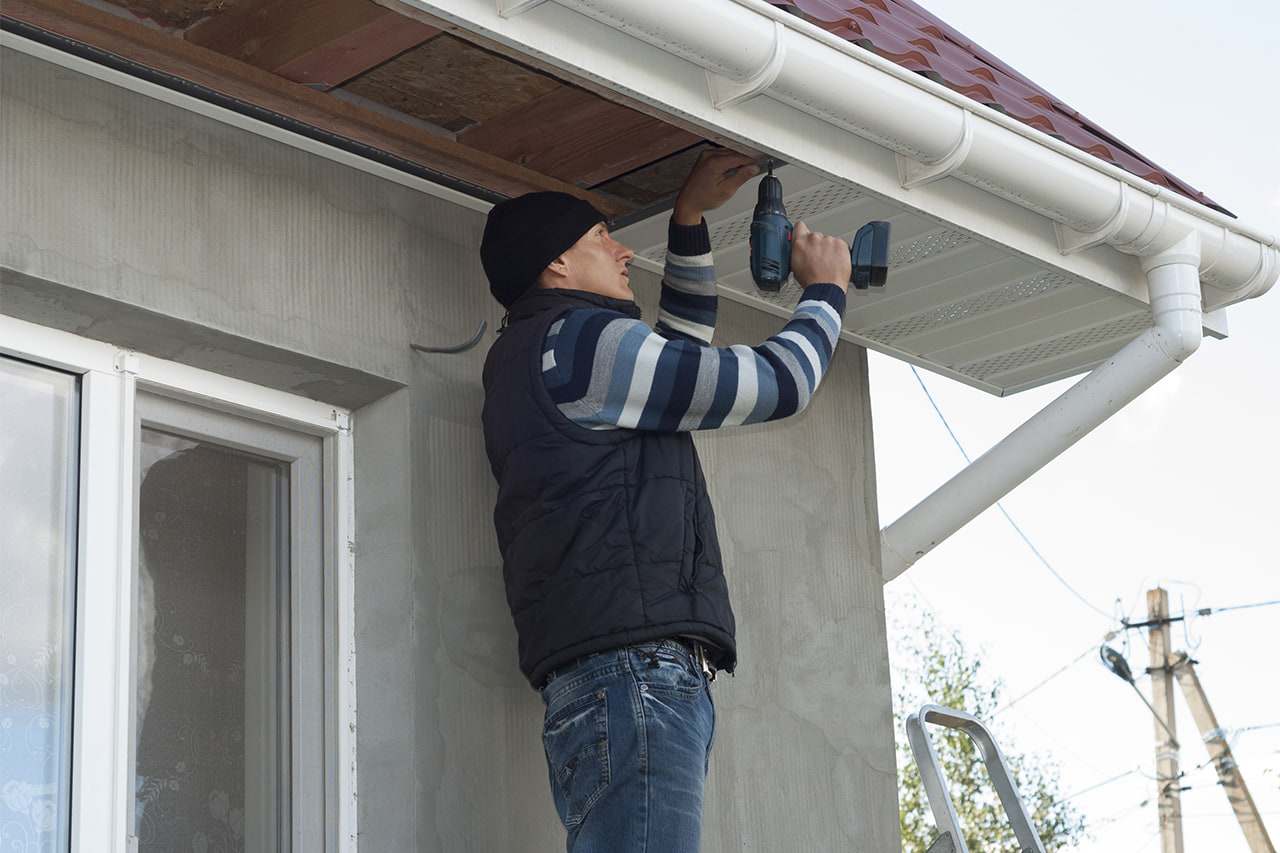 Roofline fitter screwing a ventilated white uPVC soffit board into place beneath the gutter