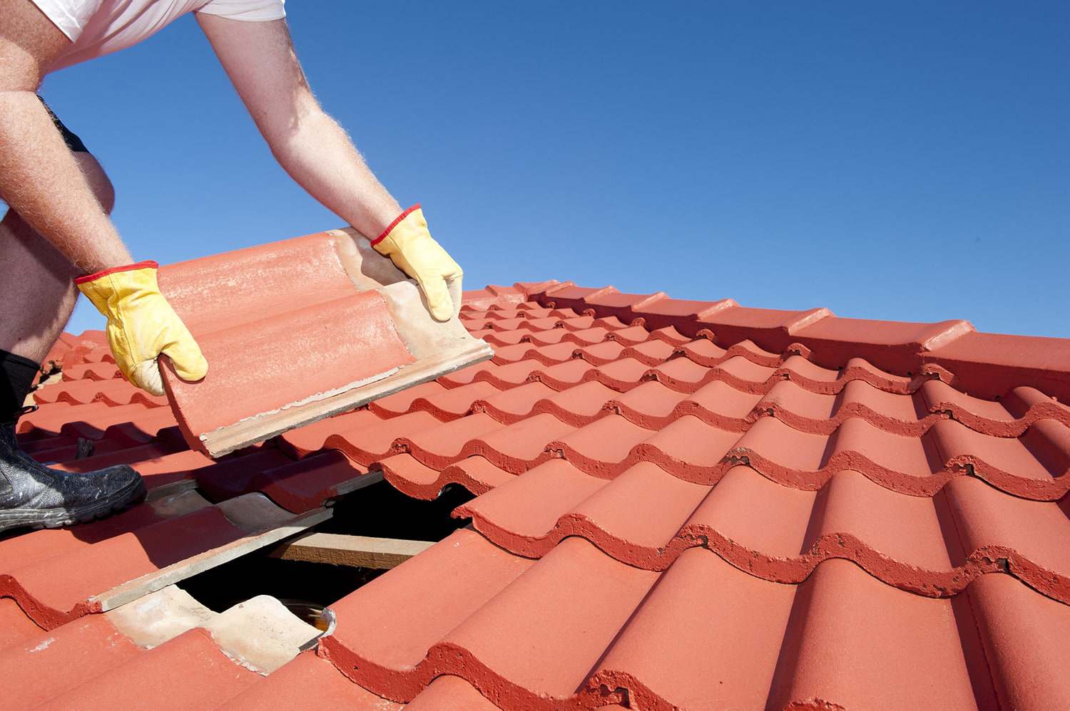 Roofer in work gloves lifting a red interlocking roof tile to reach the battens underneath