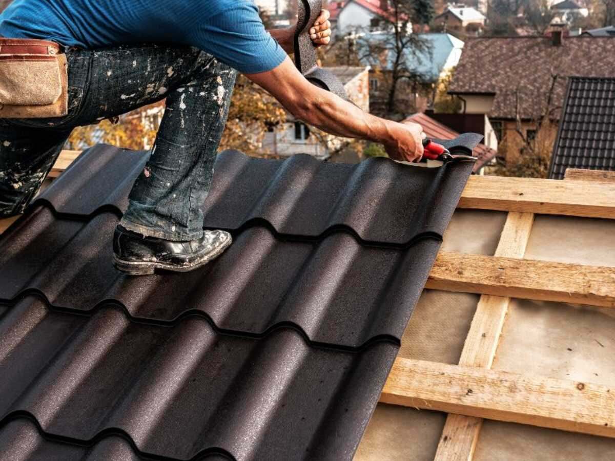 Roofer trimming a dark tile-effect roof sheet laid over new battens and membrane