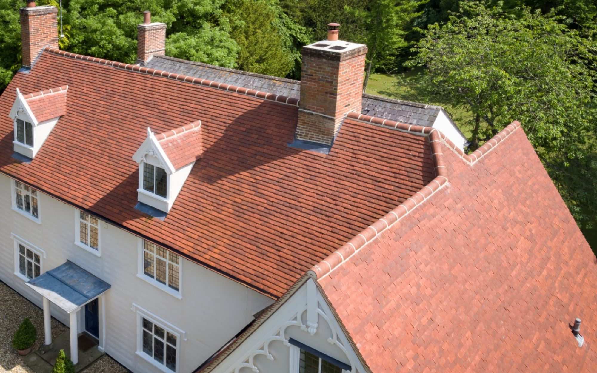 Aerial view of a white weatherboarded house with a red clay plain tile roof, gabled dormers and brick chimneys