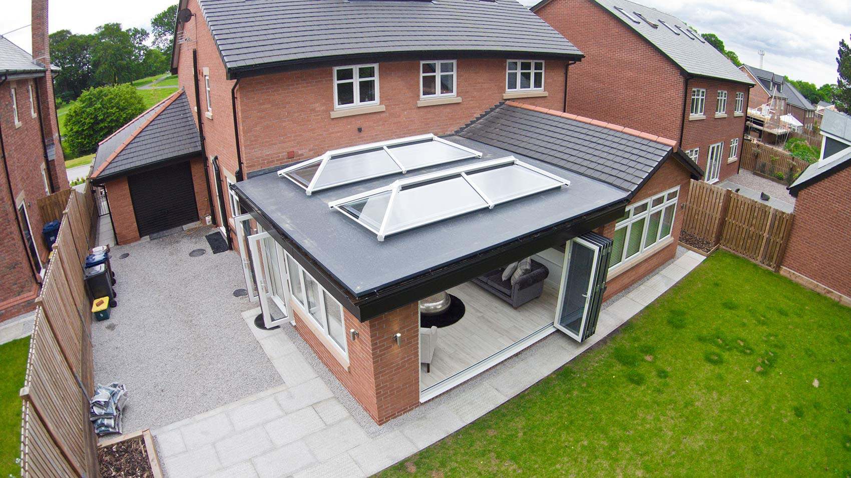 Flat-roofed rear extension with two glass roof lanterns and bifold doors on a red-brick house