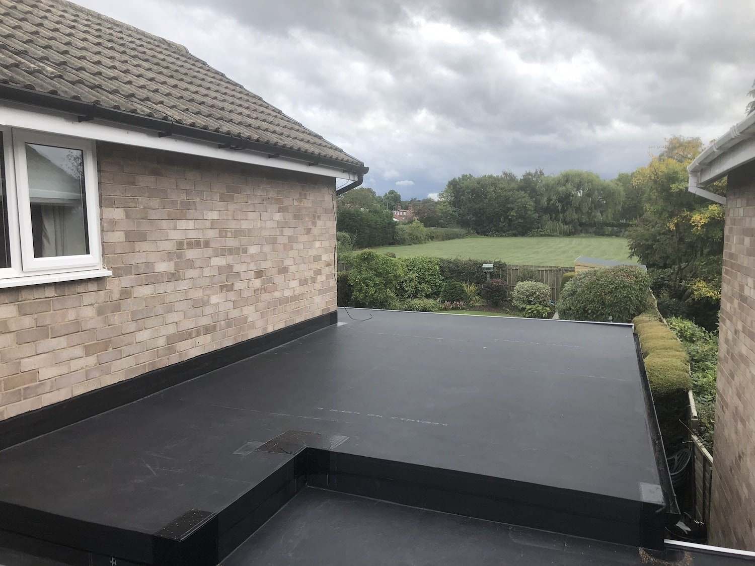 Newly finished dark flat roof membrane on a single-storey extension beside a pale brick house