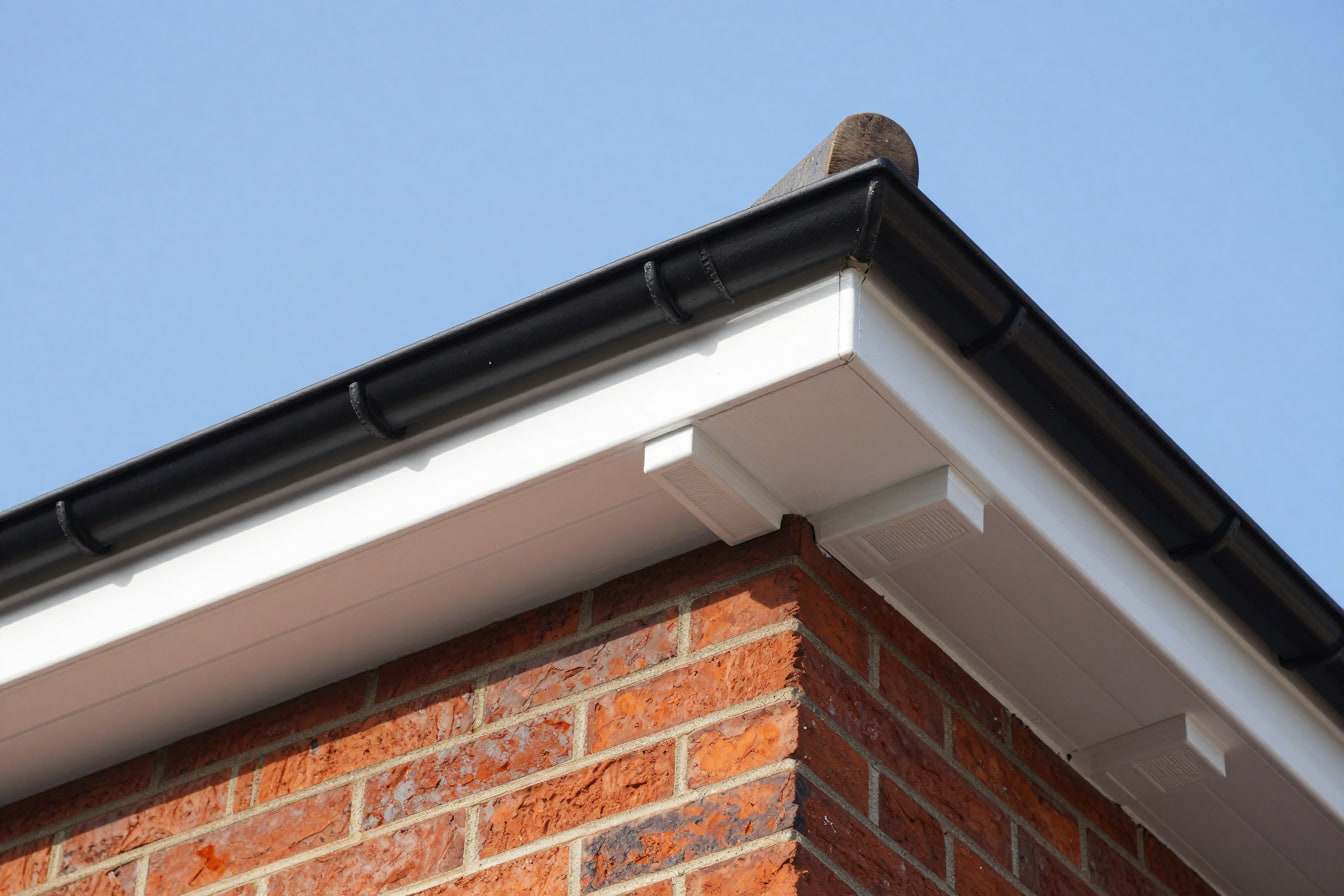 White uPVC fascia and soffit with eaves vents under a black half-round gutter on the corner of a red brick house