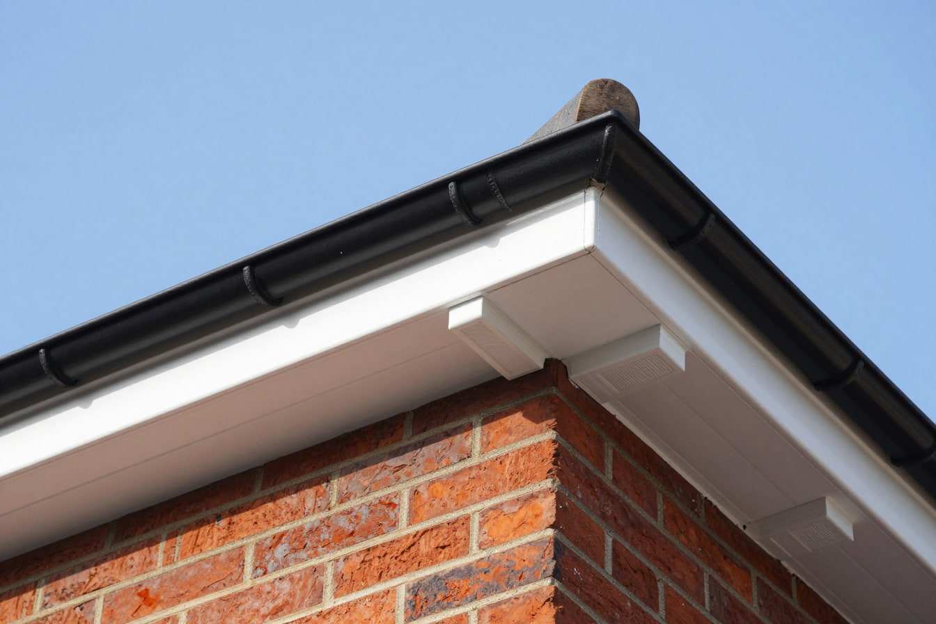 White uPVC fascia and soffit with eaves vents under a black half-round gutter on the corner of a red brick house