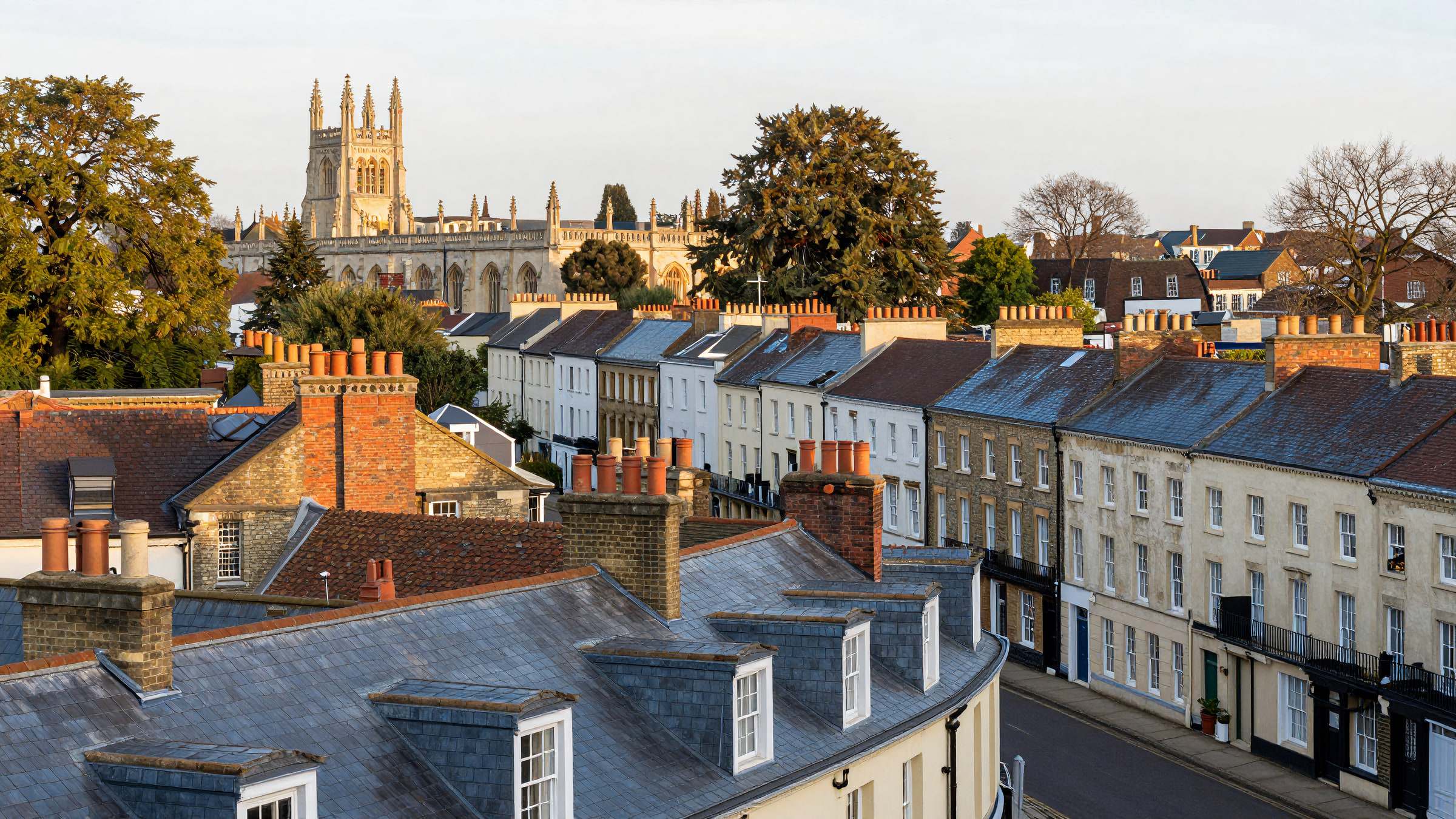 Rooftops of a Cambridge street of Victorian terraces with chimney stacks and college towers on the horizon